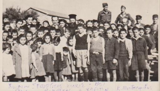 [Κιλκίς, φωτογραφία]: Χωρίον Σπουργίτης Κιλκίς - Τα παιδιά του σχολείου(;) με τον ιερέα, τον δάσκαλο, στρατιώτες και την Έλλη Γεωργίτσα [αρχηγό της Παιδοπόλεως Αγίας Τριάδος Θεσσαλονίκης, 1948-1950)], ασπρόμαυρη, διαστάσεις 15Χ10.5, στο πίσω μέρος σημειώνονται με στυλό τα ονόματα των τριών παραπάνω προσώπων και διατυπώνονται ευχές για το Πάσχα
