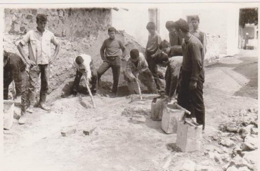 [Γεωργικά, Αρέθουσα Θεσσαλονίκης]:  Φωτογραφία ασπρόμαυρη - στο πίσω μέρος της σημειώνεται: "Αγροτόπαιδες Σχολείου Γεωργ. Τεχνικής Αρεθούσης εκπαιδευόμενοι εις την τέχνην του οικοδόμου υπό ειδικού τεχνίτου", διαστάσεις 18Χ12