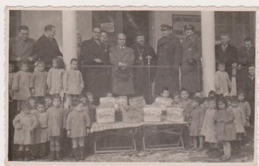 [Χαλκιδική, Πολύγυρος]: Φωτογραφία ασπρόμαυρη, διαστάσεις 14Χ9, ο εικονιζόμενος στο κέντρο Μητροπολίτης Κασσανδρείας Καλλίνικος [Χαραλαμπάκης], σημειώνει με μελάνι στο πίσω μέρος "Μάρτιος - Απρίλιος 1954, Πολύγυρος * Παιδικός σταθμός, 1955", [πιθανόν διανομή Αμερικανικής βοήθειας στα παιδιά]